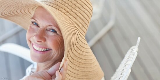 Smiling middle-aged woman wearing broad-brimmed hat looking over shoulder
