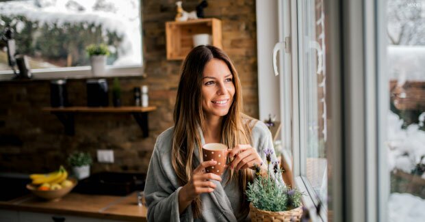 Young woman holding a cup while looking out a window